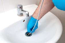 Plumber using drain snake to unclog drain.