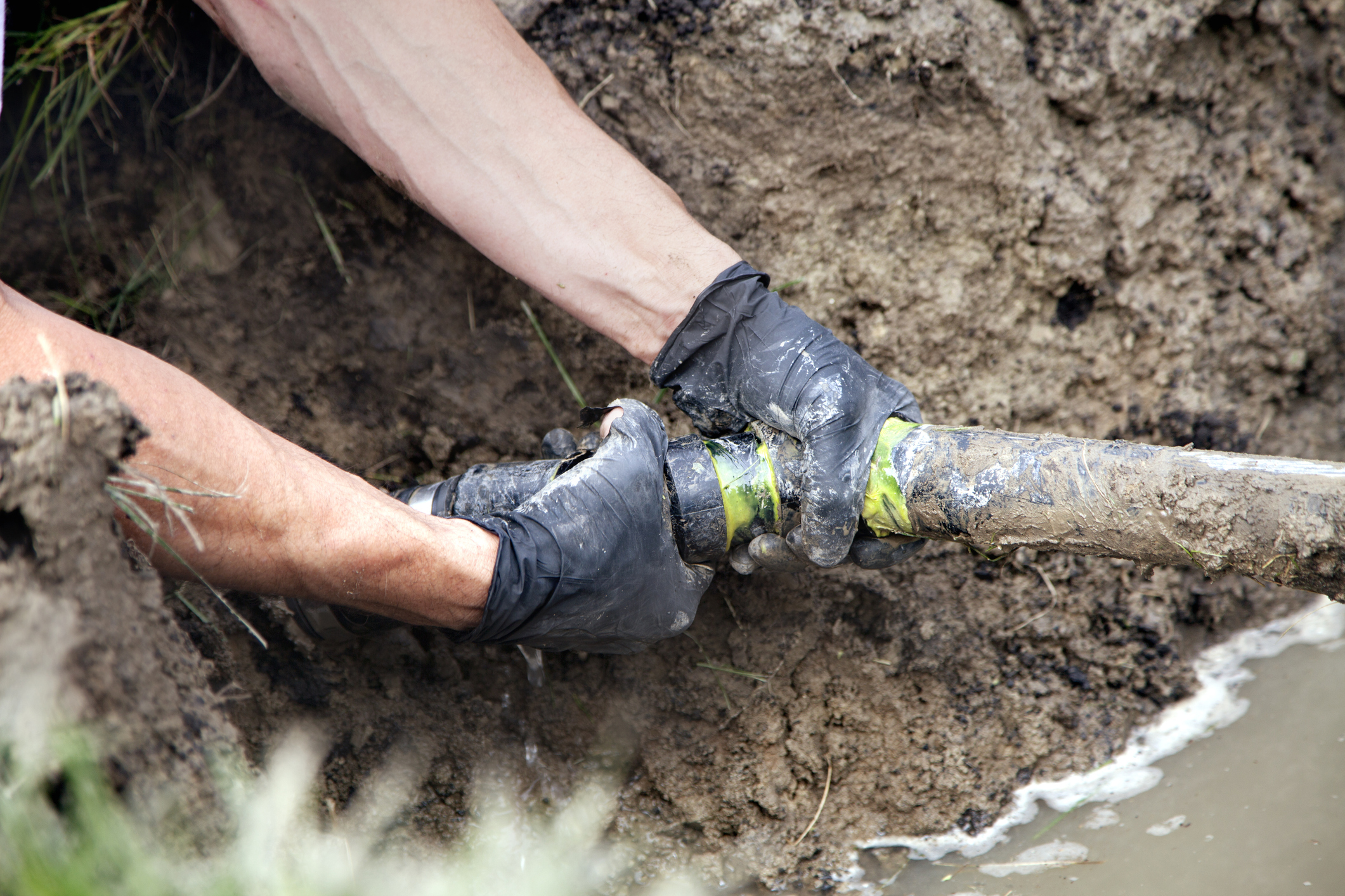Pair of hands with black gloves grabbing a dug-up sewer pipe.